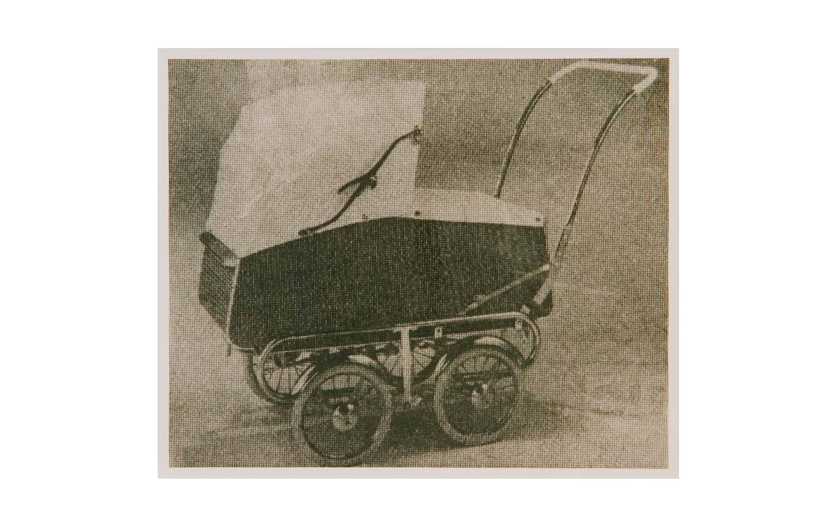 Historischer Kinderwagen mit Stoffverdeck, Metallrahmen und vier Rädern ruht vor neutralem Hintergrund.