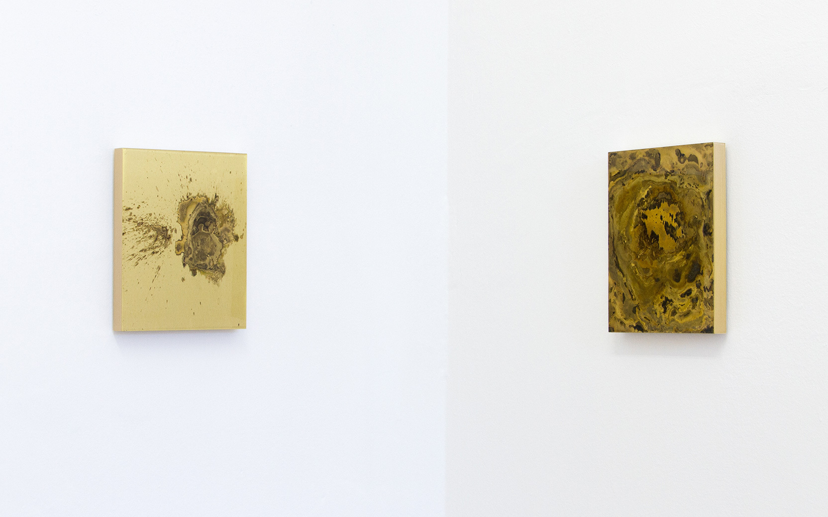 Two small abstract canvases hung on a white gallery wall; left beige with brown blot, right dark yellow-brown marbled swirl.