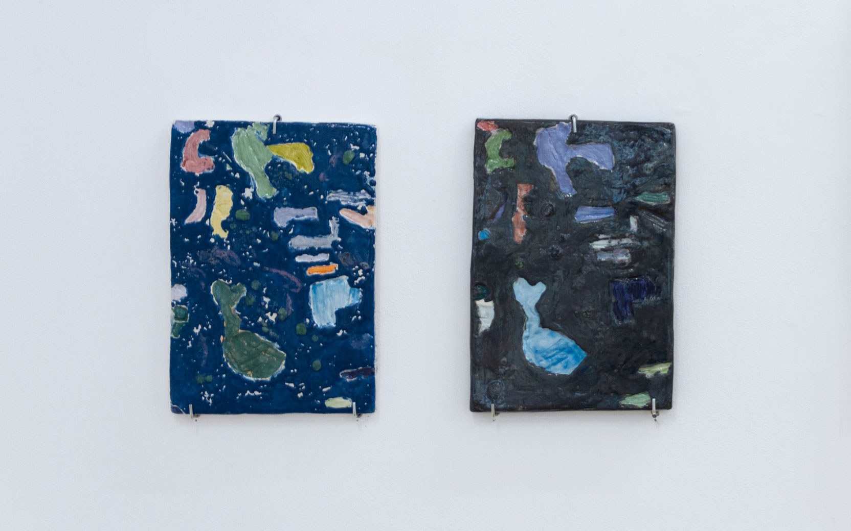 Two rectangular abstract paintings hung on a white wall; left panel cobalt blue with multicolored shapes, right panel dark gray with blue patches.